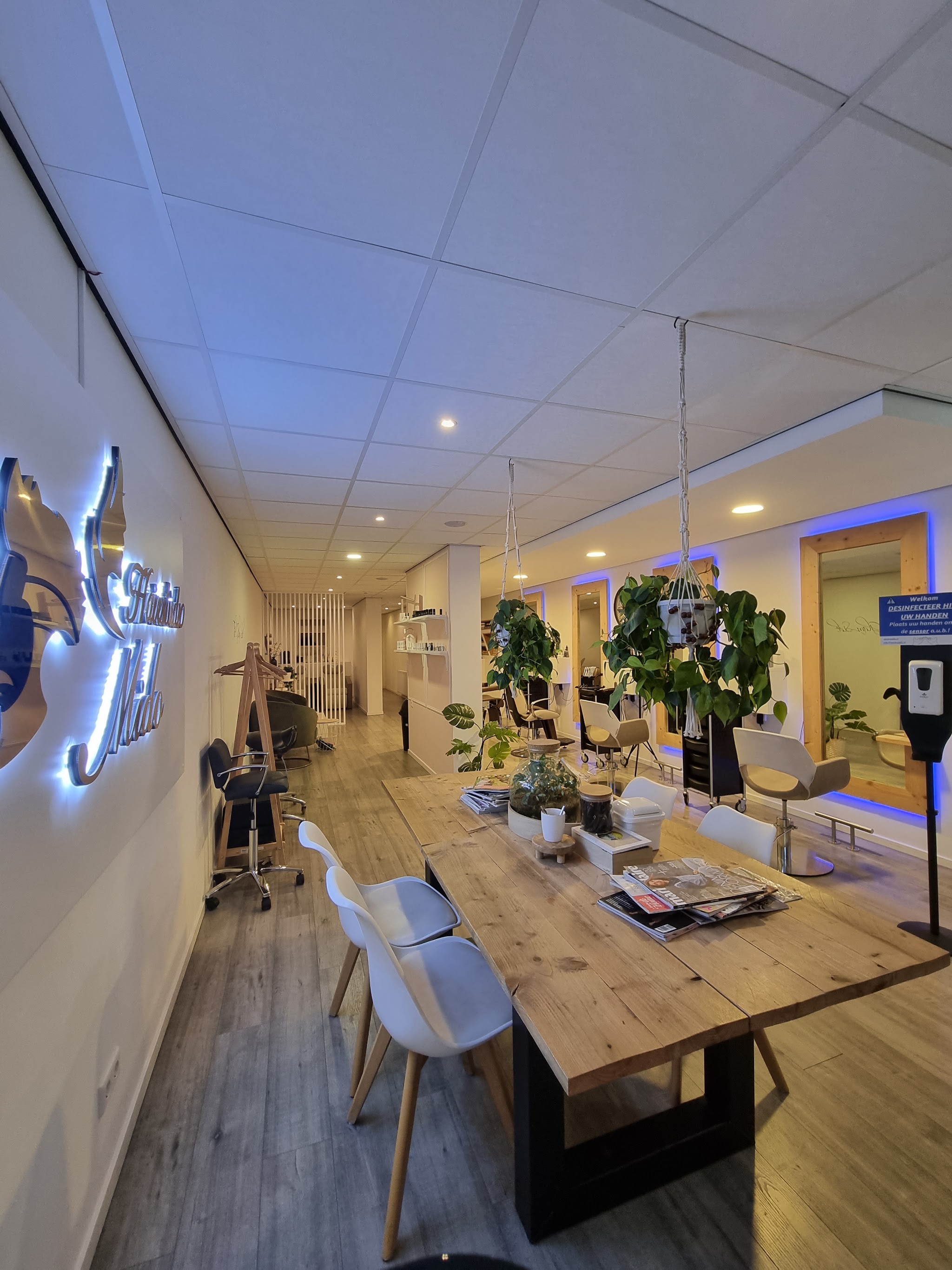 Het verlichte logo van Hairstudio Mido aan de muur boven de lange houten tafel