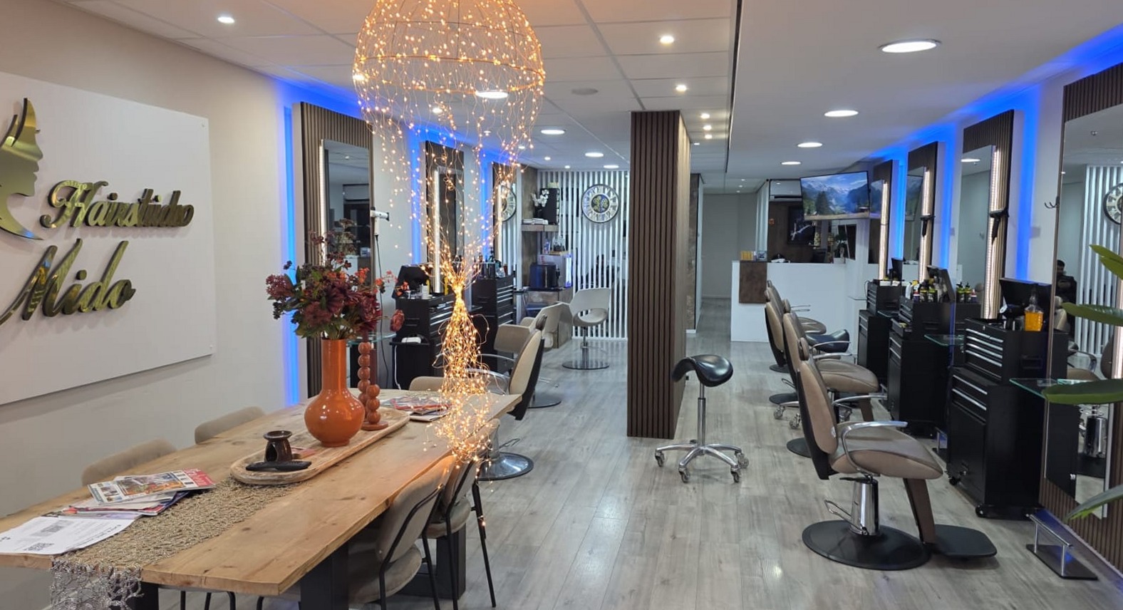 De salon van Hairstudio Mido met het gouden naambord aan de muur, de lange tafel en de spiegels met blauwe verlichting